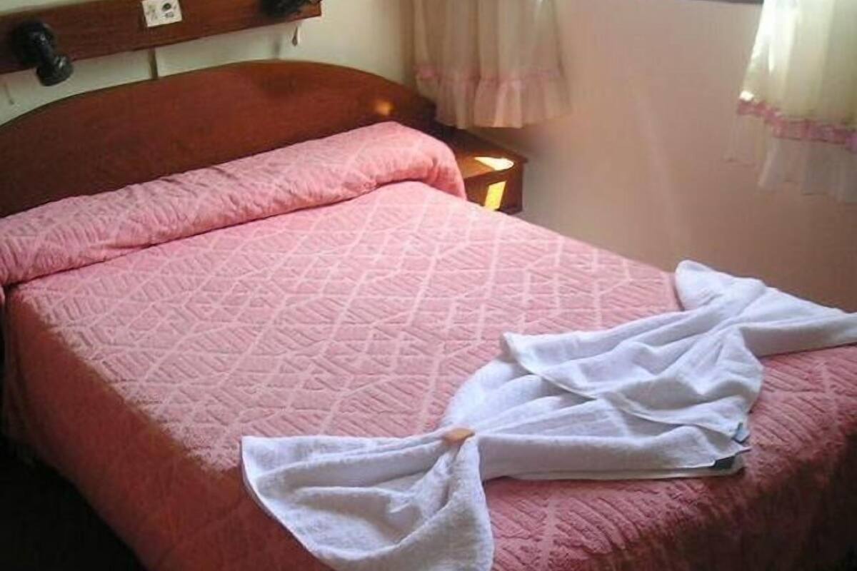 Un lit recouvert d’une couette rose et sur lequel sont pliées des serviettes blanches.