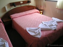 A single bed with a pink quilt and a white towel folded on top.