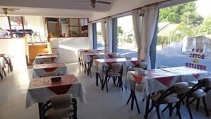 Un comedor con mesas y sillas, ventanas amplias con cortinas y vistas al exterior.