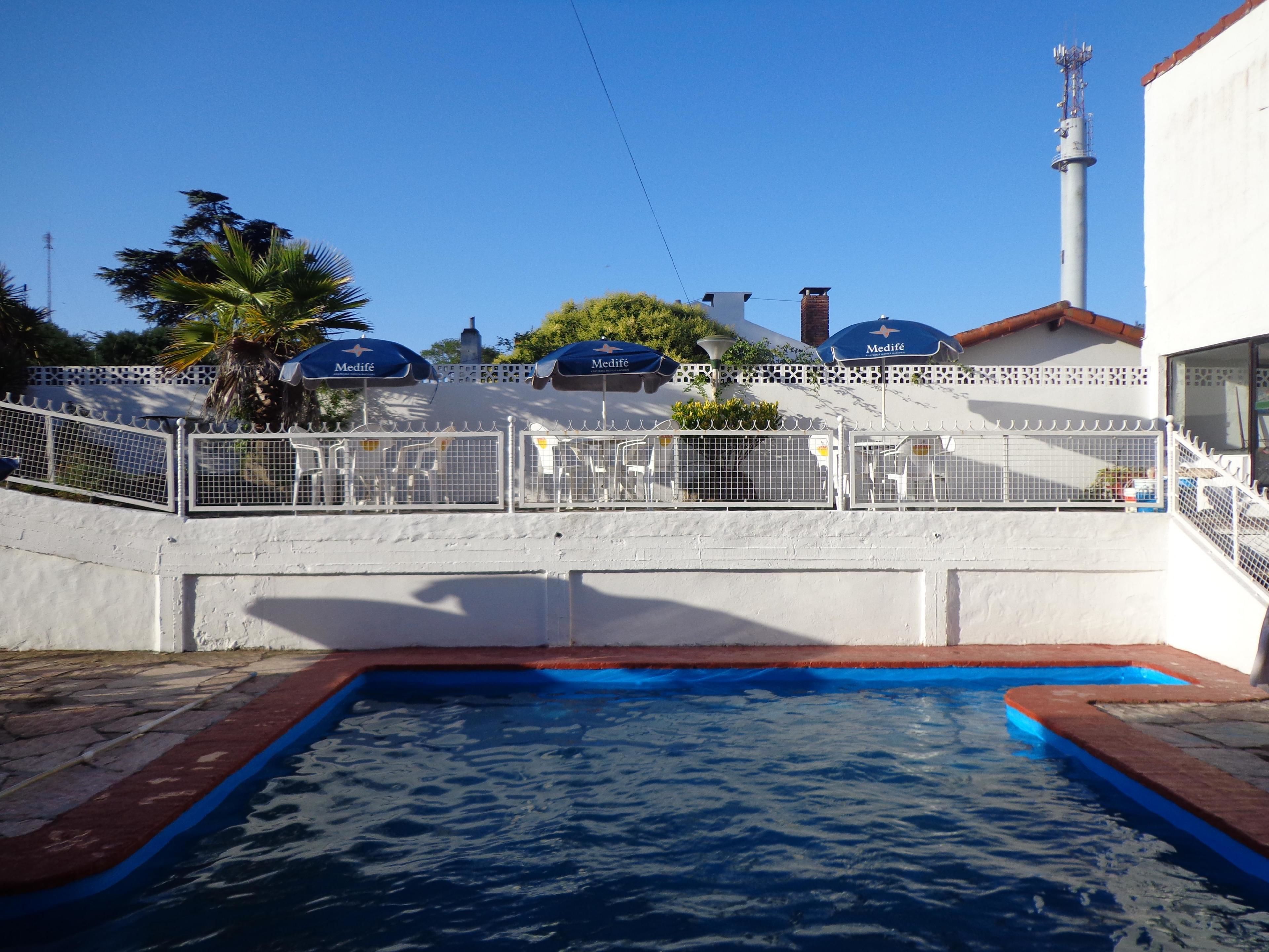 Uma piscina com cerca branca e guarda-sóis azuis identificados com 'Medife'.