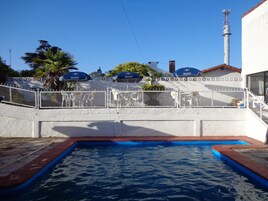 Uma piscina com cerca branca e guarda-sóis azuis identificados com 'Medife'.