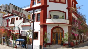 A hotel with a red and white facade, multiple balconies, and outdoor seating. - Hotel Bristol (Termas de Rio Hondo)