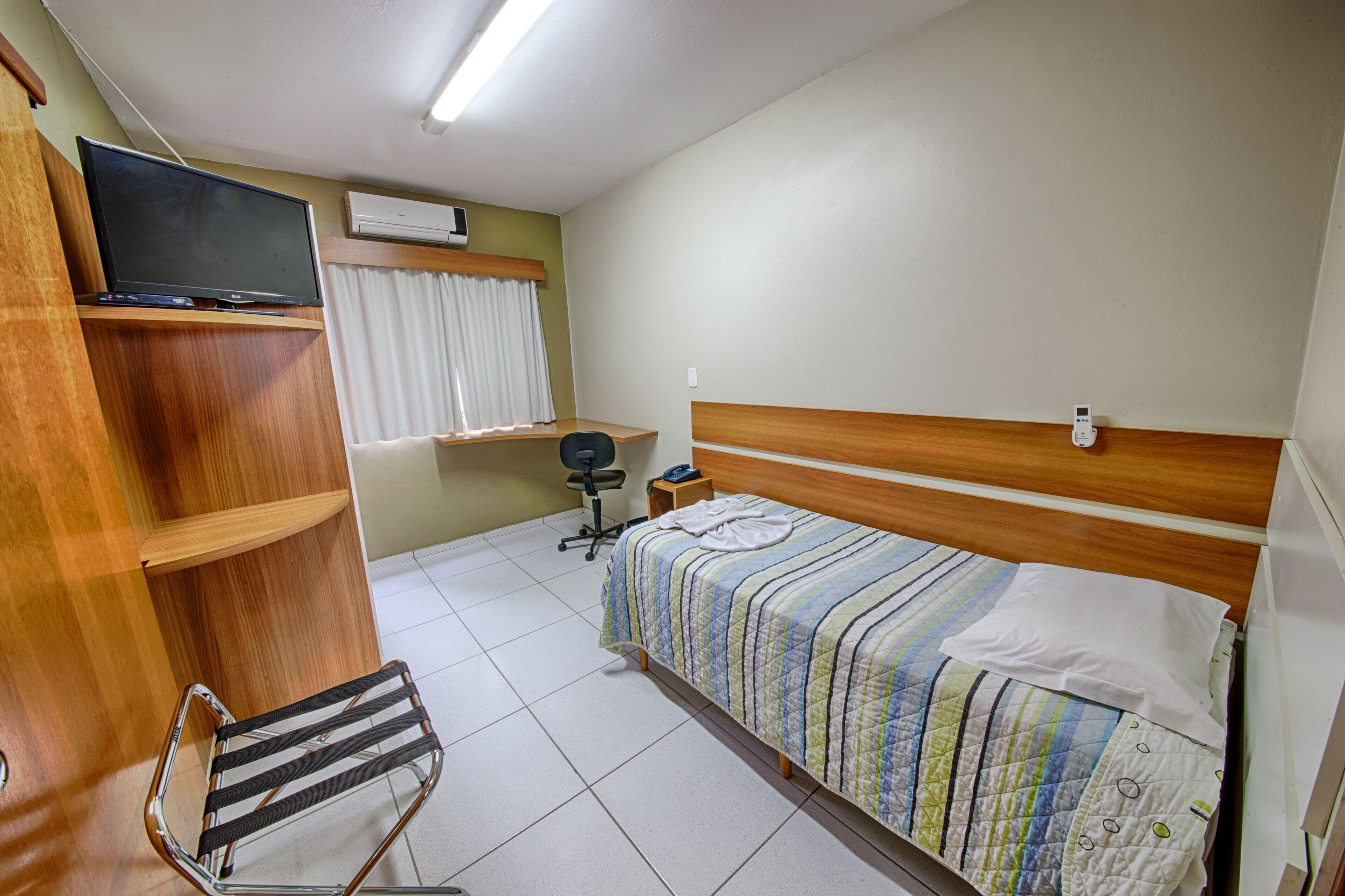 Habitación de hotel con cama, escritorio, silla, televisor y aire acondicionado.