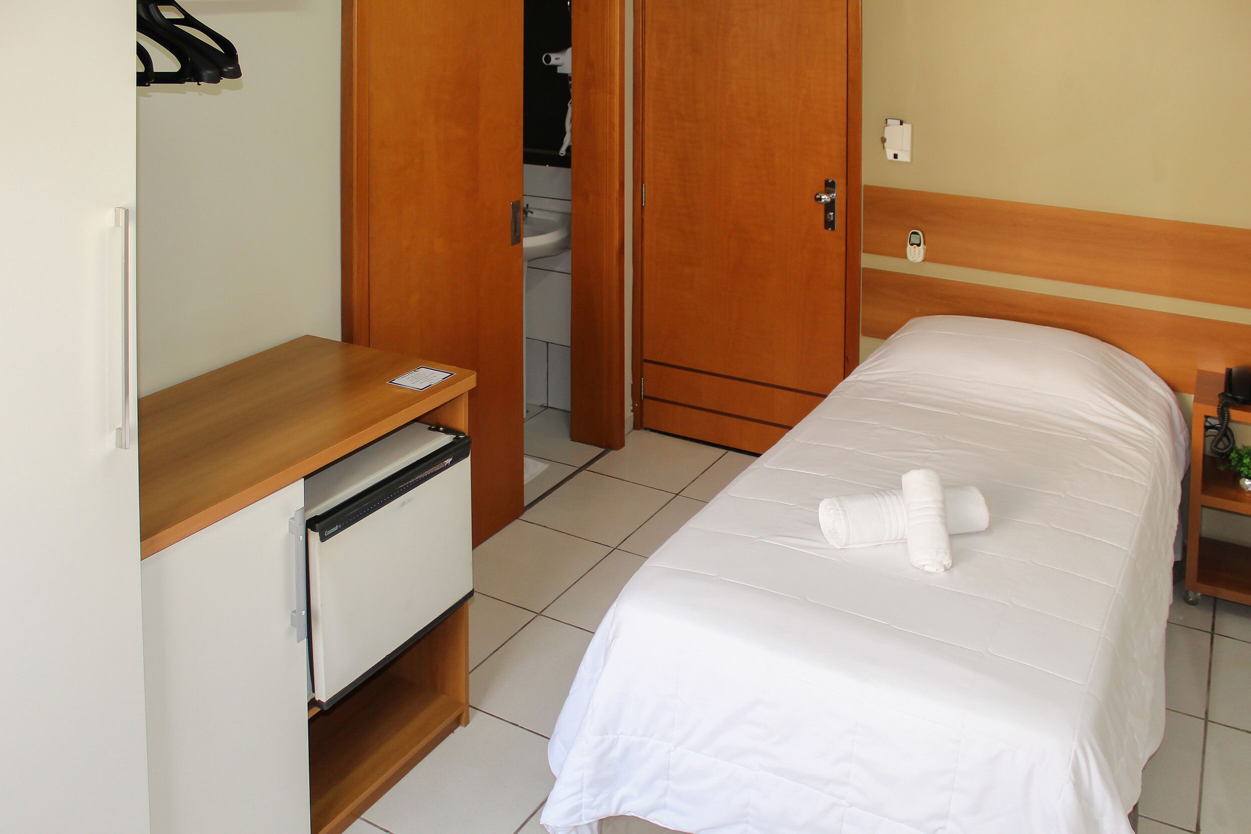 A hotel room with a bed, a wooden desk, a white cabinet, and a door leading to a bathroom.