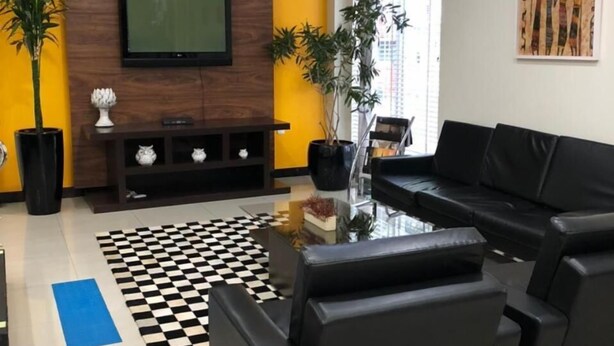 Una sala de estar moderna con un sofá de cuero negro, una mesa de centro de vidrio, un tapiz a cuadros y un televisor de pantalla plana montado en una pared de madera.