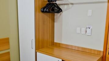A compact bedroom with a bed, a wardrobe, a small desk, and a shelf.