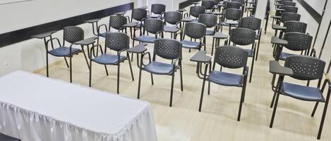 Konferenssitila, jossa on riveissä tuoleja ja pöytiä, yhdellä pöydällä valkoinen pöytäliina ja seinillä musta reunus.