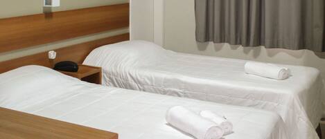 A hotel room with two beds, a wooden headboard, a nightstand, and a window with curtains.