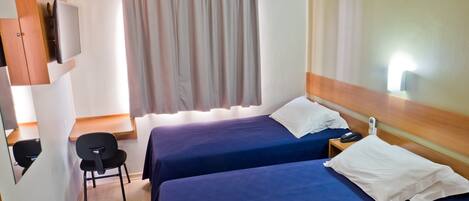 Habitación de hotel con dos camas, una silla, un escritorio con computadora y televisión.