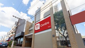 Un hotel llamado 'Tri Centro' con un gran letrero rojo, fachada de ladrillo y el reflejo de un árbol visible en las ventanas.