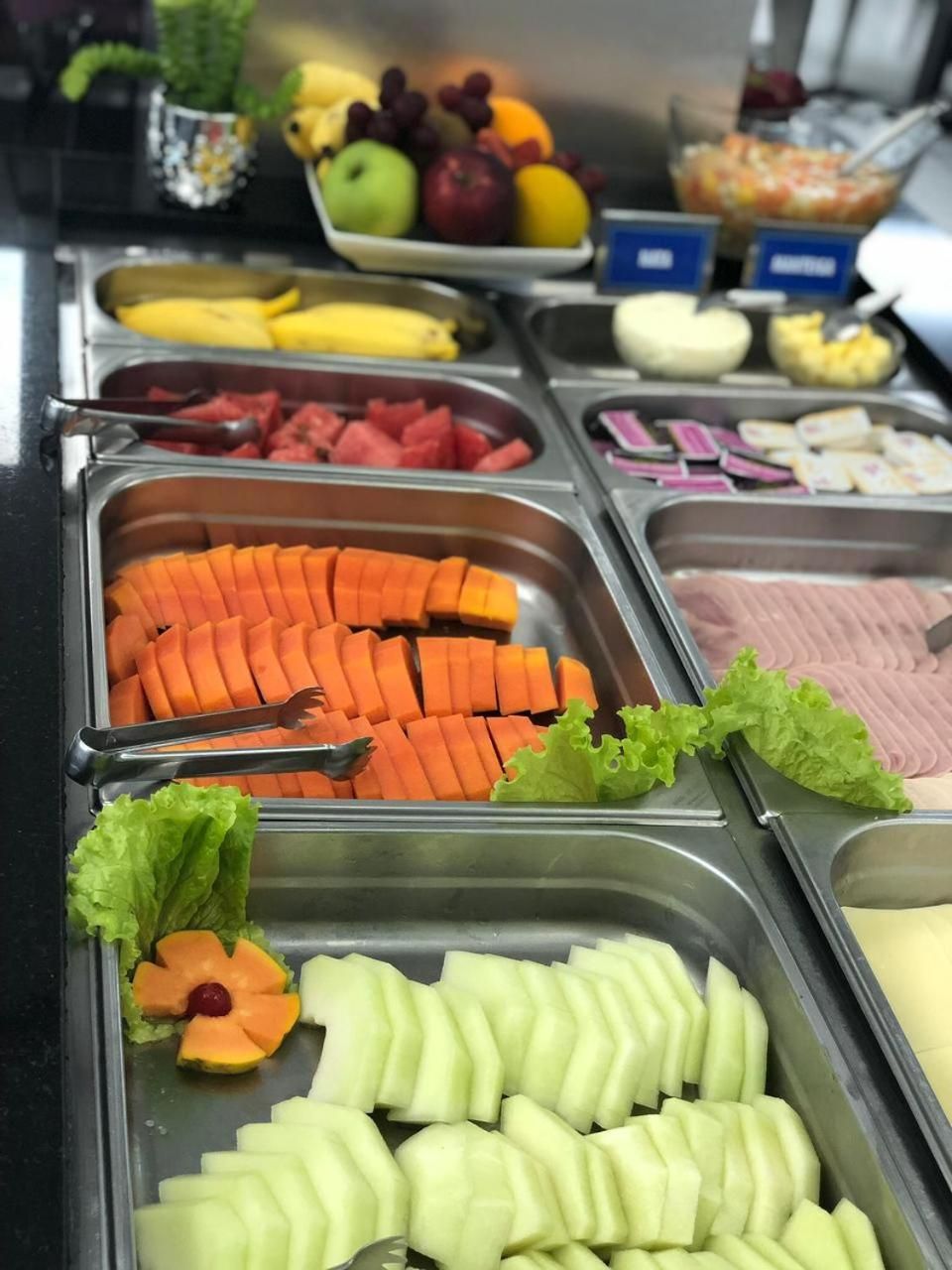 Un bufé con diferentes opciones de comida, como frutas cortadas, verduras y carnes.