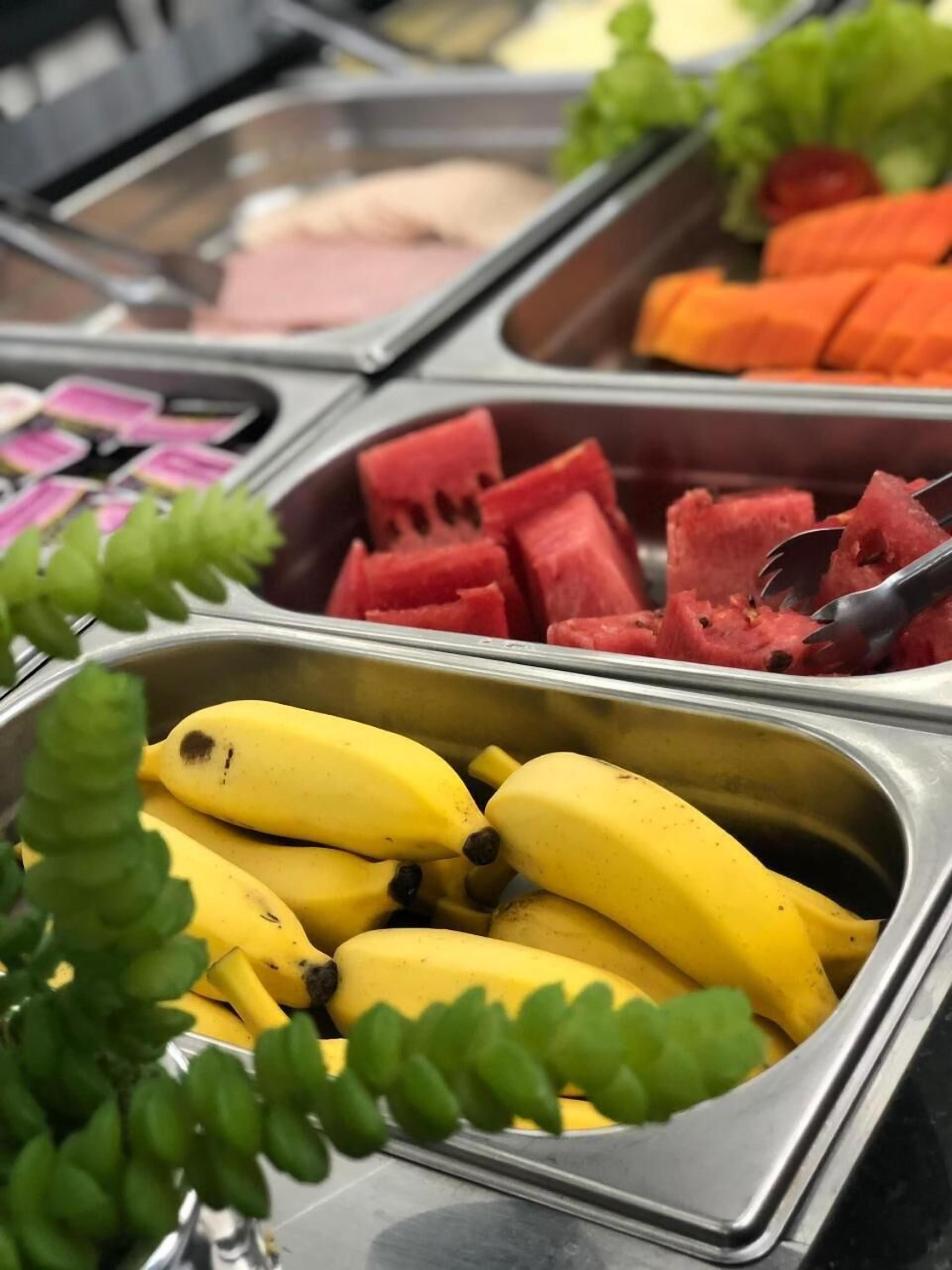 A buffet with various fruits and vegetables, including bananas, watermelon, and carrots.
