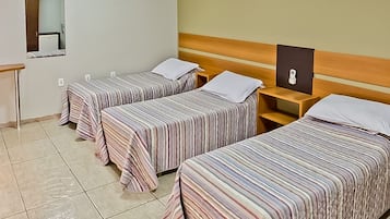 Une chambre d’hôtel avec trois lits simples, une tête de lit en bois, une petite table de chevet avec une lampe et un miroir au mur.