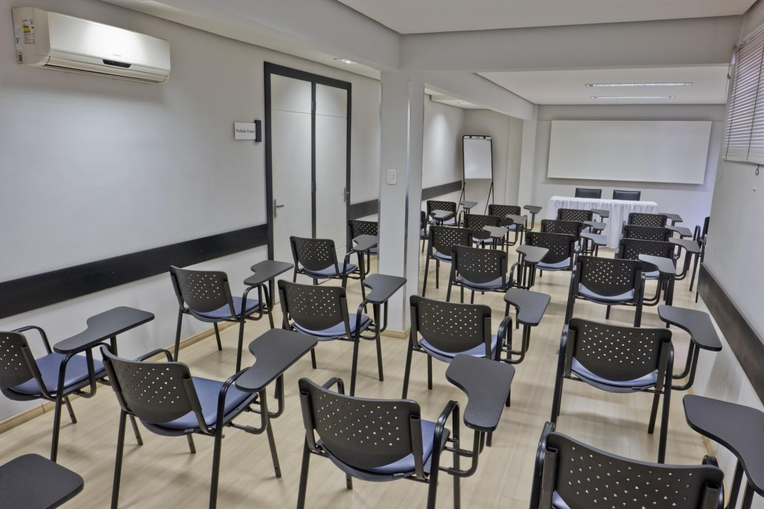 Una aula amb files de taules i cadirees, una pissarra i una pantalla projectora.