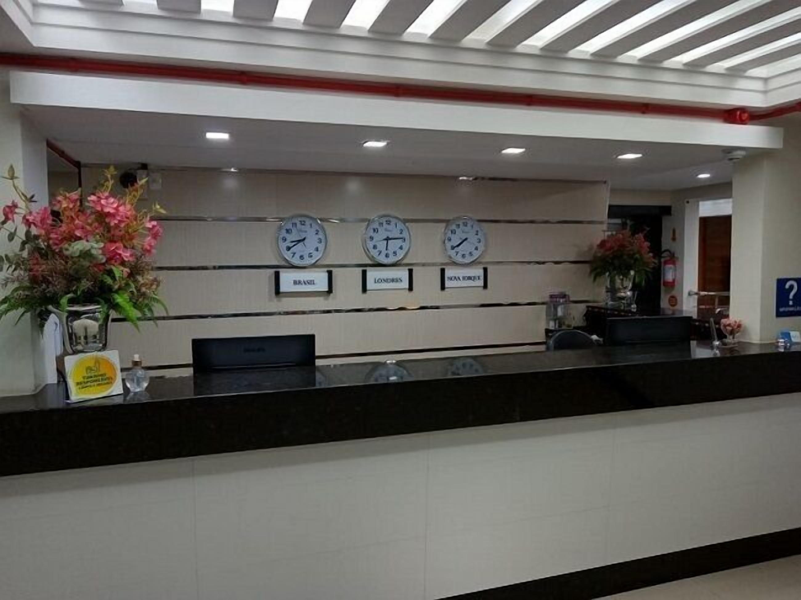 A reception desk with three clocks labeled Brazil, London, and Nova Orleje.