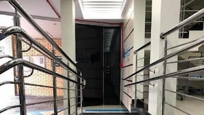 Un pasillo con barandillas metálicas, un camino táctil azul y un techo con luces lineales.