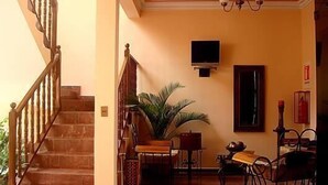 A staircase leading to a landing with a wooden railing, a potted plant, a television mounted on the wall, and a dining area with metal chairs and a table. - Hostal Santa Teresa de Jesús (Sucre)