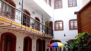 A courtyard with a balcony, arched doorways, and a colorful umbrella. - Hostal Santa Teresa de Jesús (Sucre)