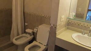 A bathroom with a bidet, toilet, sink, and a glass shower enclosure.