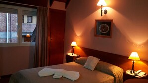 A hotel room with a bed, two bedside lamps, a window with curtains, and a framed picture on the wall.