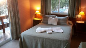 A hotel room with a bed, two bedside lamps, a window with a view, and a towel on the bed.