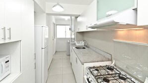A modern kitchen with white cabinetry, a granite countertop, a gas stove, and a microwave. - Wasi Apartments Atahualpa (Lima)