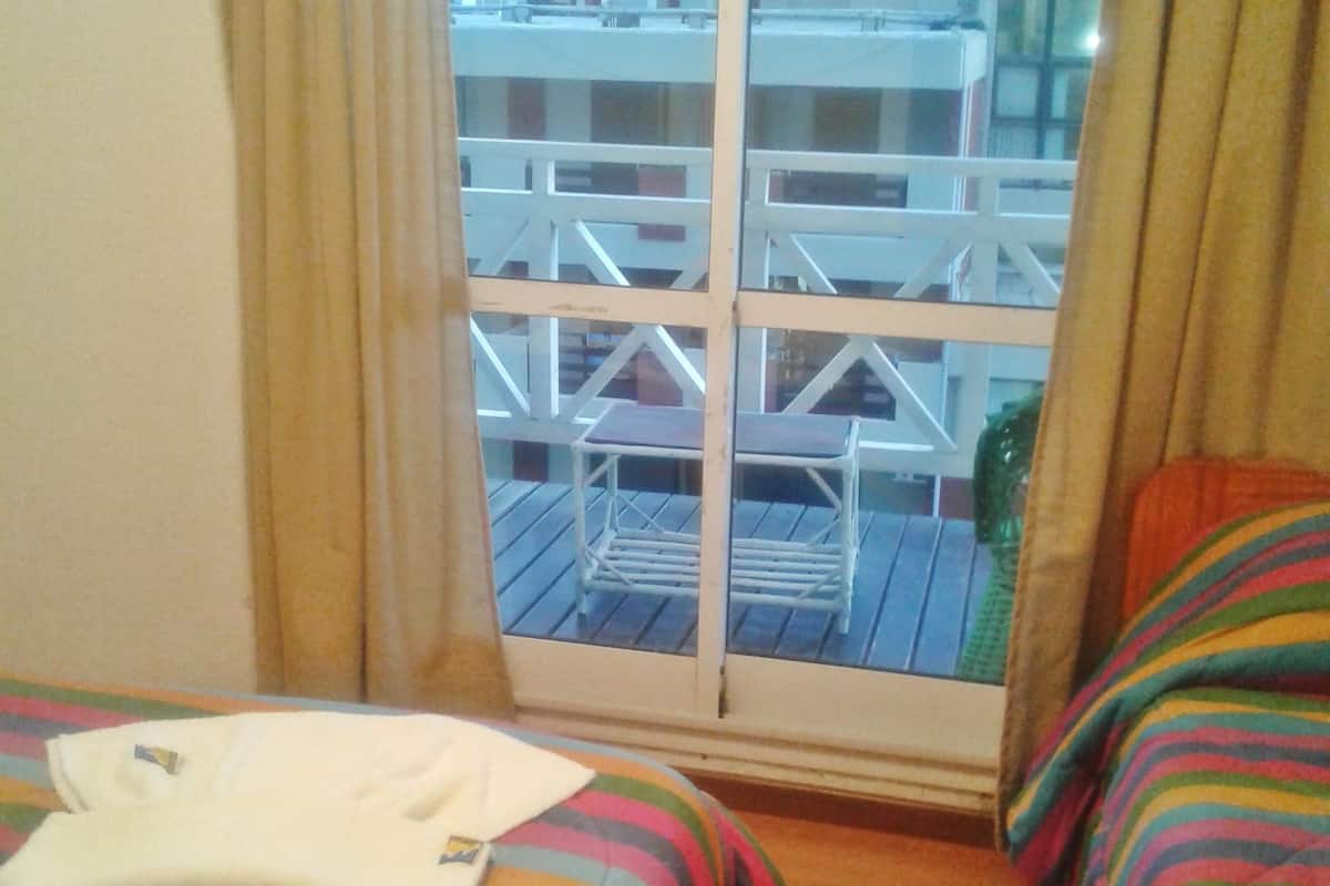 Una habitación con dos camas, una ventana con vistas a edificios y una cortina.