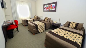 Habitación de hotel con dos camas individuales, un escritorio con silla, televisión y ventana con cortinas.
