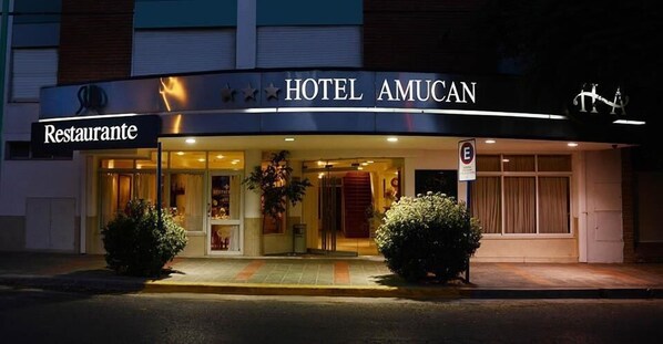 Un hôtel avec une enseigne indiquant la présence d’un restaurant, une entrée bien éclairée et un panneau interdisant le stationnement.