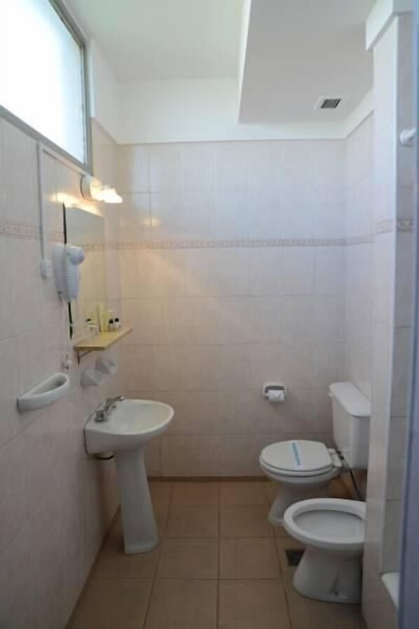 Un baño pequeño con lavamanos, dos inodoros y un espejo.