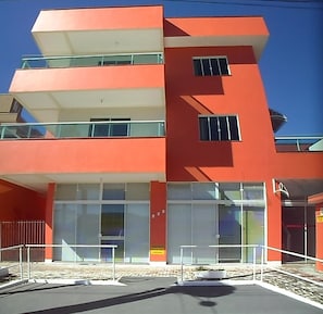 A modern building with a red facade, multiple balconies, and large windows. - Recanto do Sossego Residence (Bombinhas)