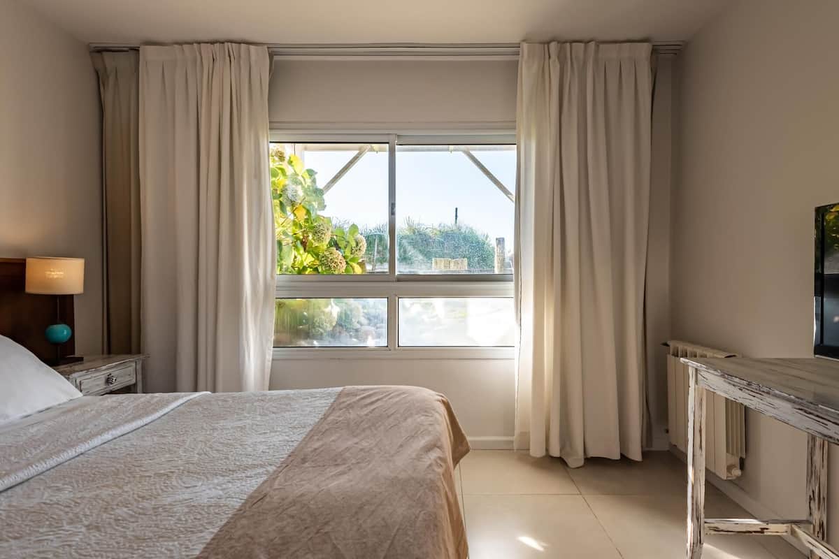 Quarto com uma cama, mesa de cabeceira com abajur, cômoda e janela com cortinas.