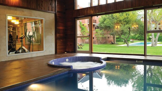 Área de spa com hidromassagem e equipamentos de ginástica, grandes janelas com vista para um quintal.