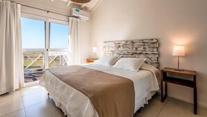 Quarto com cama grande, ventilador de teto, janela com cortinas e vista para o exterior.