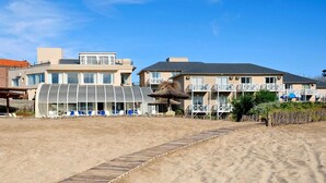 Um hotel à beira-mar com fachada de vidro, área de estar ao ar livre e calçada de areia.