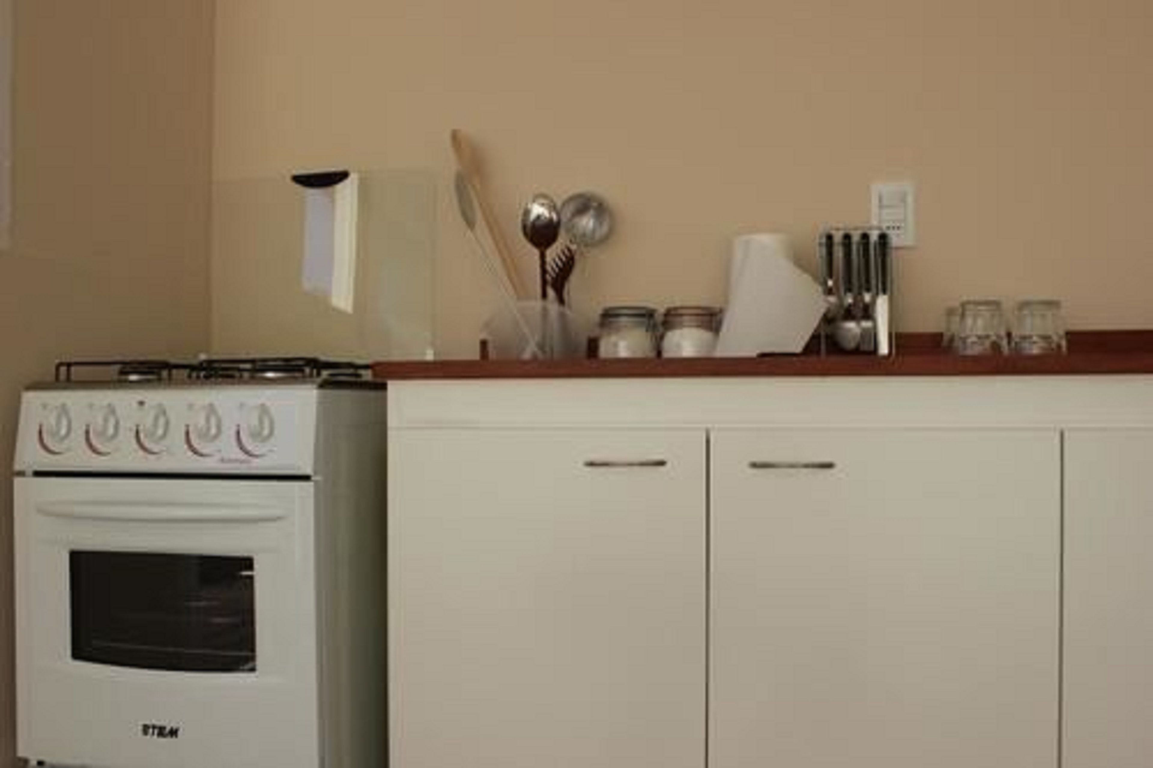 Una cocina con horno blanco y alacenas, una encimera con utensilios y un microondas instalado en la pared.