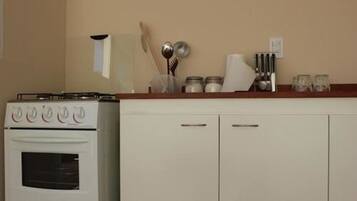 Una cocina con horno blanco y alacenas, una encimera con utensilios y un microondas instalado en la pared.