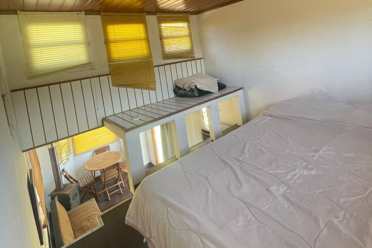 Ein Schlafzimmer mit einem Bett, einem kleinen Tisch mit Stühlen und einem Fenster mit Jalousien.