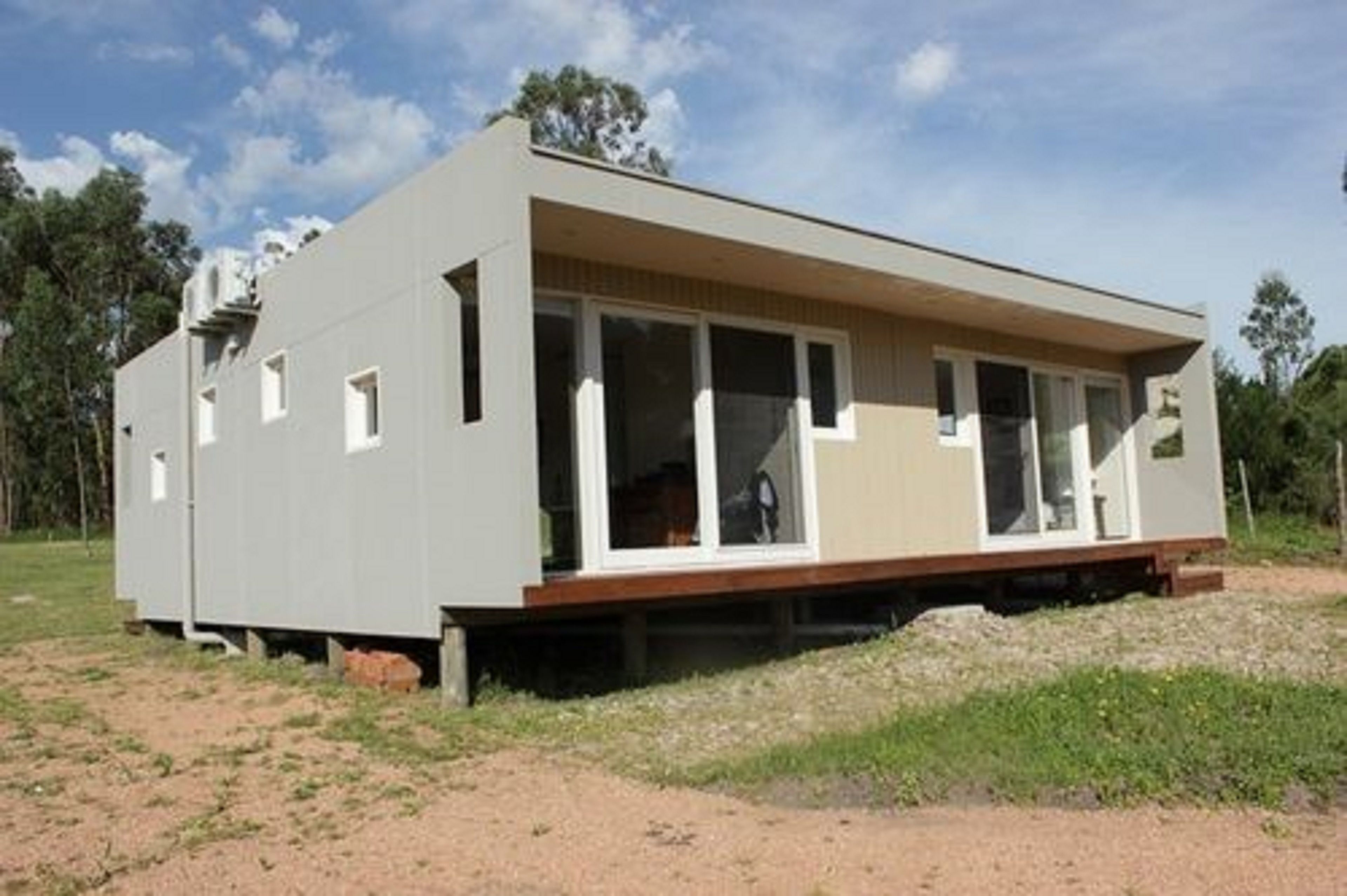 A modern, single-story building with large windows and a flat roof, situated on a grassy area with trees in the background.