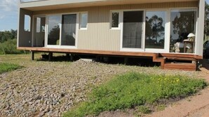 Uma casa moderna, térrea, com grandes janelas e telhado plano, localizada em um caminho de cascalho cercado por vegetação.