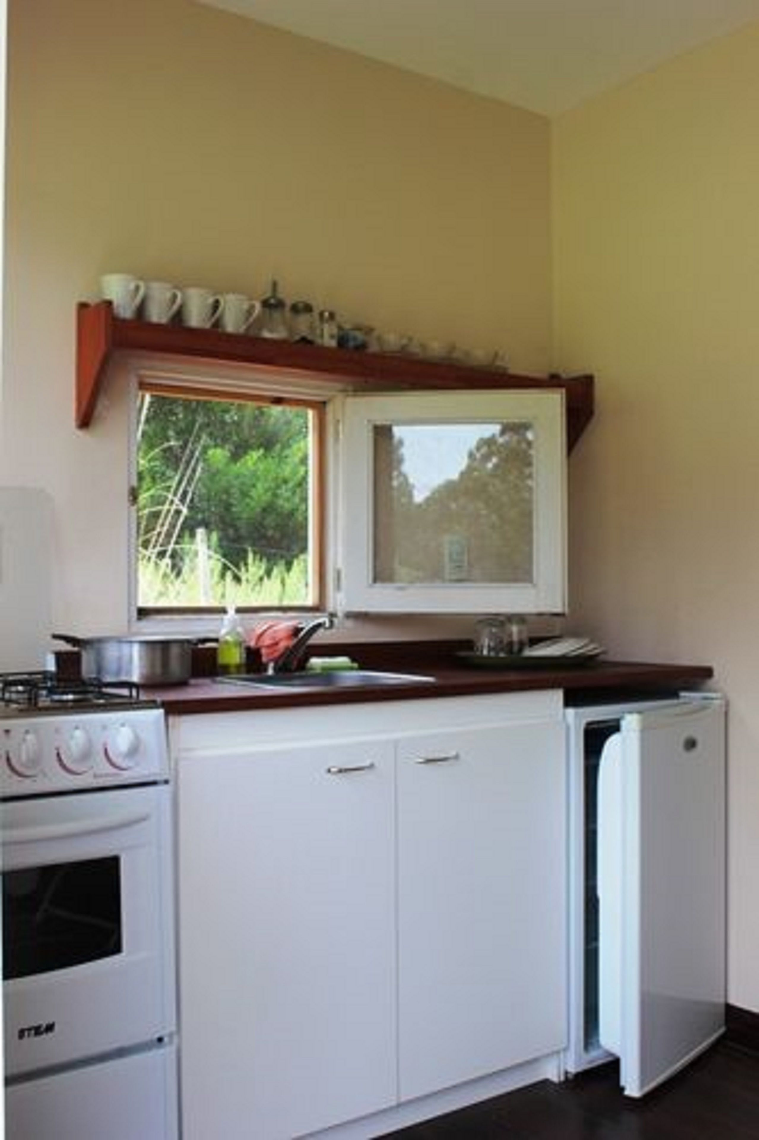Cocina compacta con estufa, horno y lavavajillas. Un ventanal ofrece luz natural y vistas al exterior.