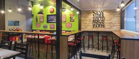A modern restaurant interior with high tables, red chairs, and green walls adorned with Coca-Cola memorabilia.