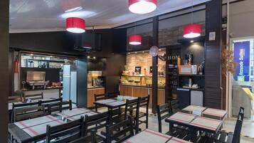 Um restaurante com mesas, cadeiras, cozinha e balcão com cardápio.