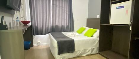 Una habitación de hotel pequeña con cama, escritorio, televisor y armario.