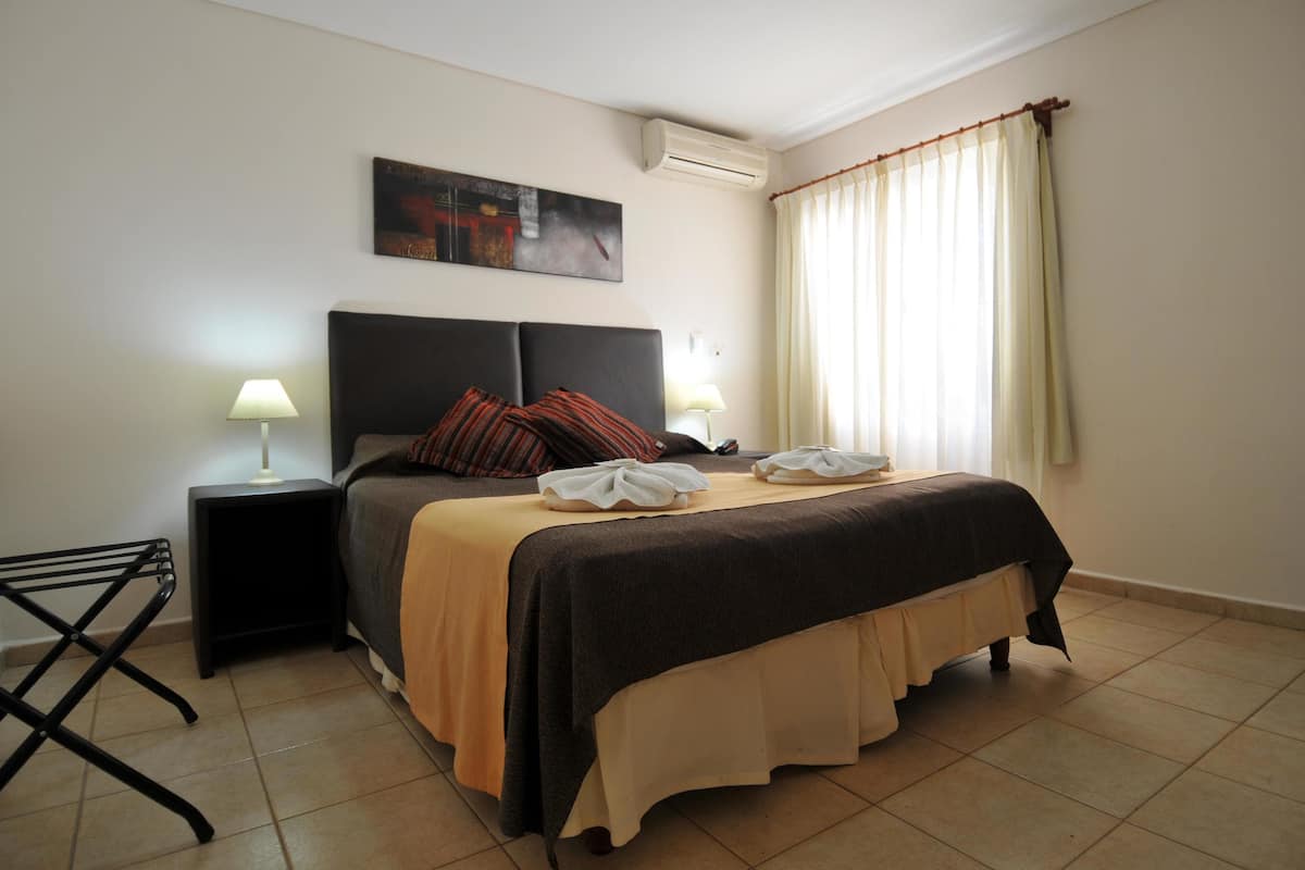 Hotelkamer met een bed, twee nachtkastjes met lampen, een wandairconditioner en een raam met gordijnen.