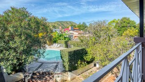 A pool area with lounge chairs, a view of a hillside with buildings, and a clear sky. - Hotel Casa Nostra (Villa Carlos Paz)