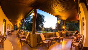 An outdoor covered seating area with chairs and tables, a bar area, and a view of trees and sky. - Hotel Yacanto (San Javier)