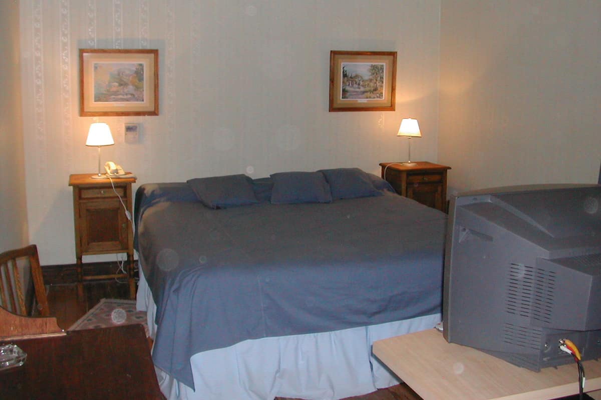 A hotel room with a bed, two bedside lamps, a television, and two framed pictures on the wall.
