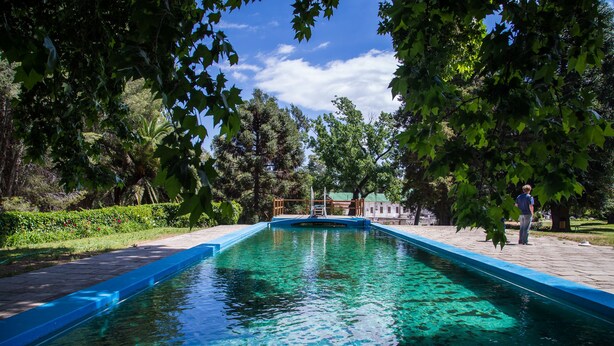 A rectangular pool with a blue edge, surrounded by trees and a paved walkway. - Hotel Yacanto (San Javier)