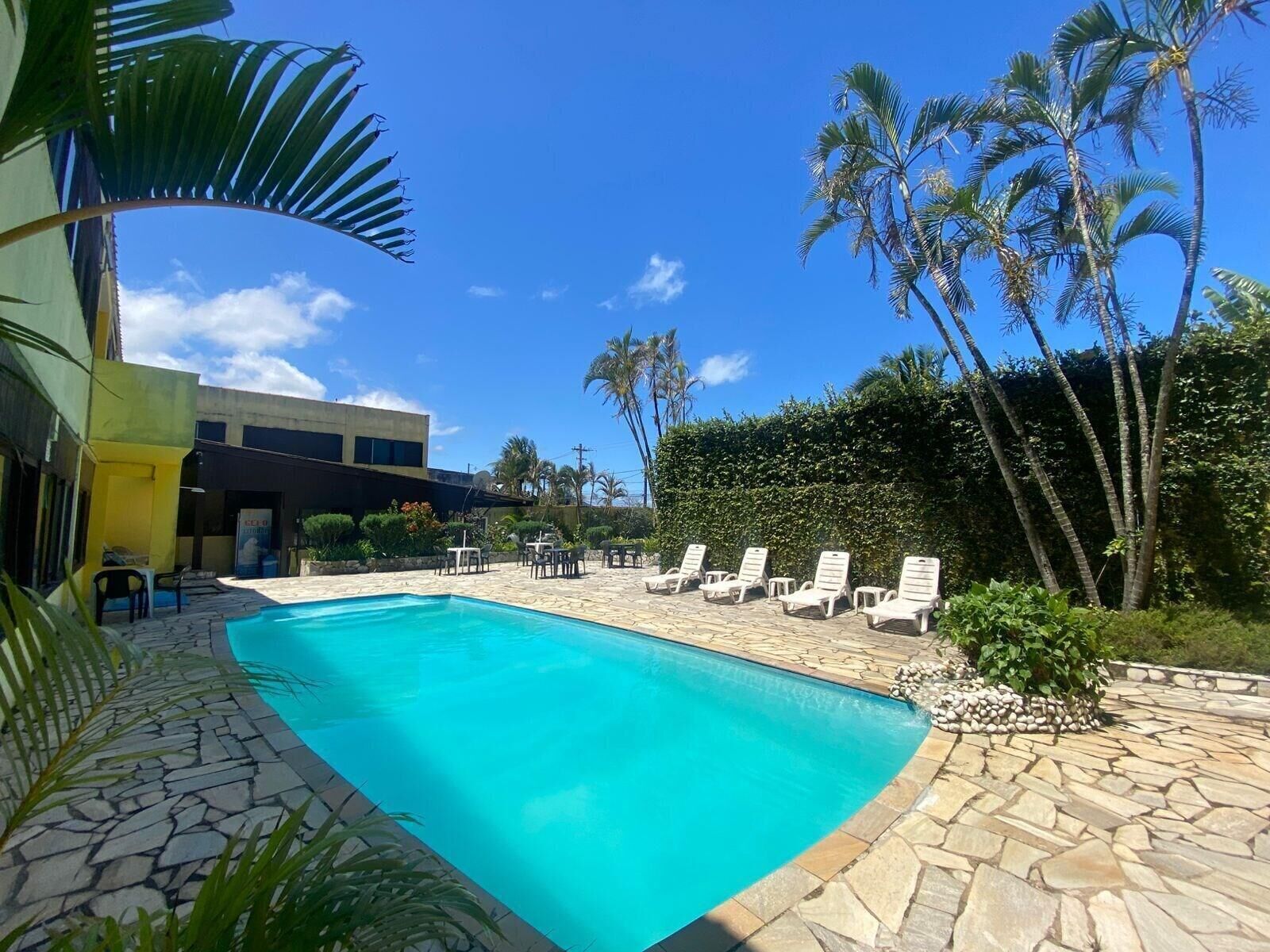 A swimming pool with lounge chairs, palm trees, and a building in the background.